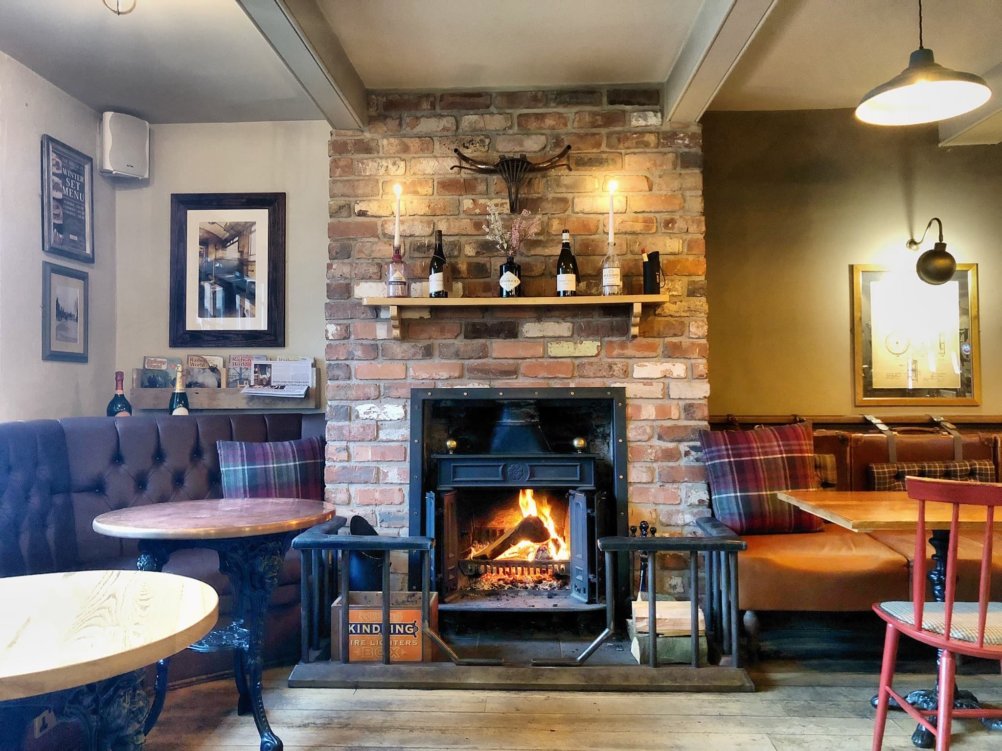 The Railway pub interior with a lit open fireplace, booth seating and wooden tables.