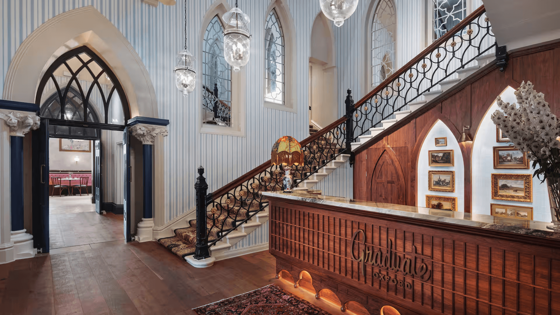 Grand hotel lobby with a carved staircase, Gothic arches and ornate ironwork balustrade.