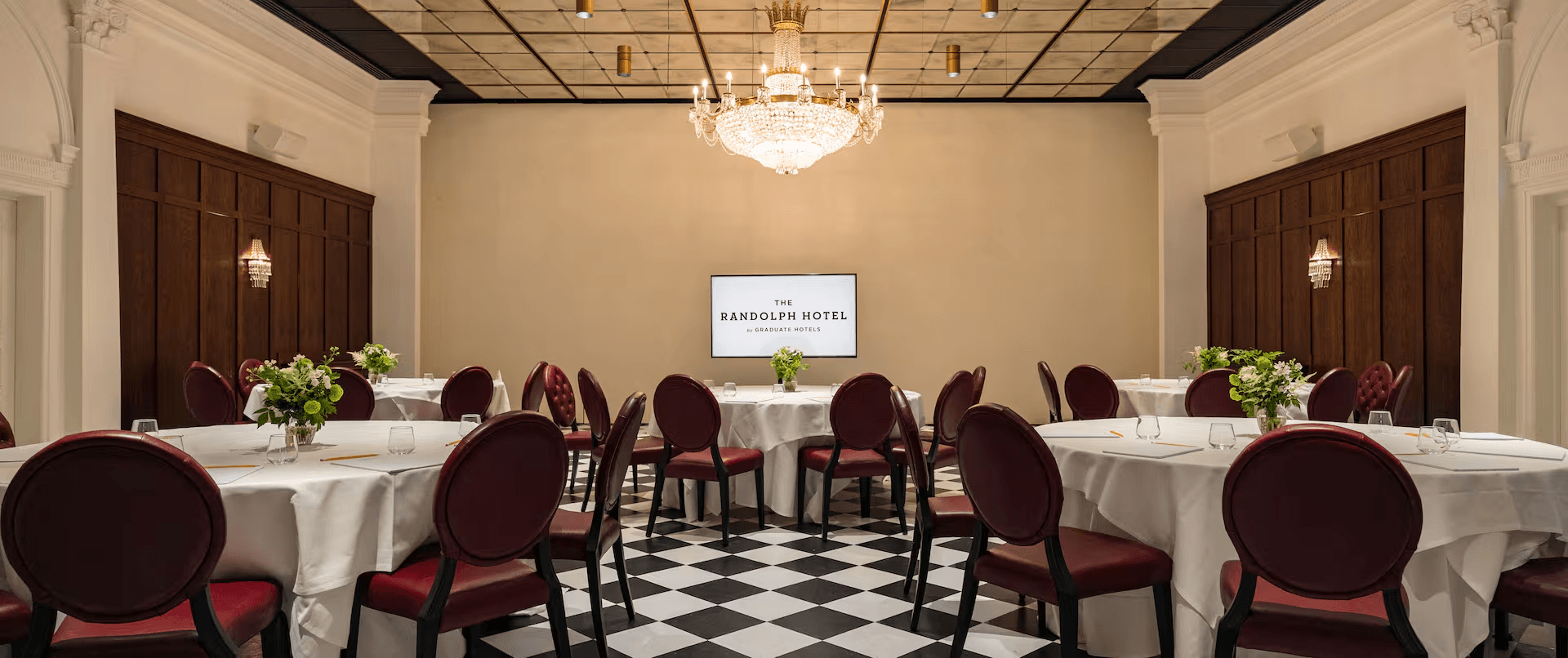 Private function room with round tables, burgundy chairs and a crystal chandelier.
