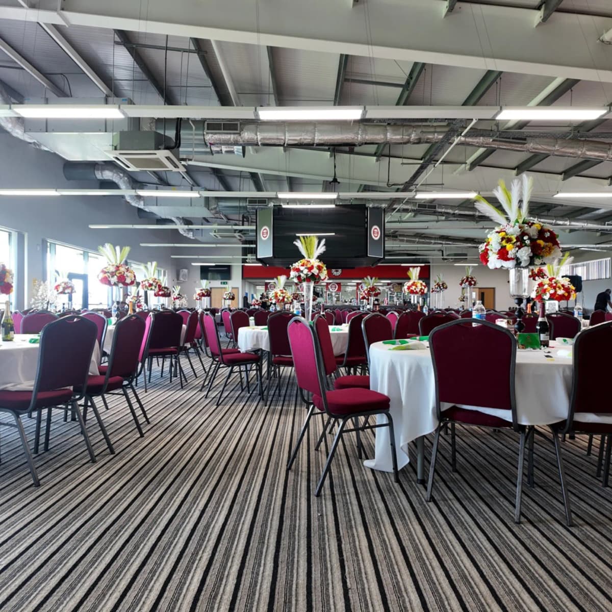 The Reddings Suite function room laid with round tables, red chairs and tall floral centrepieces.