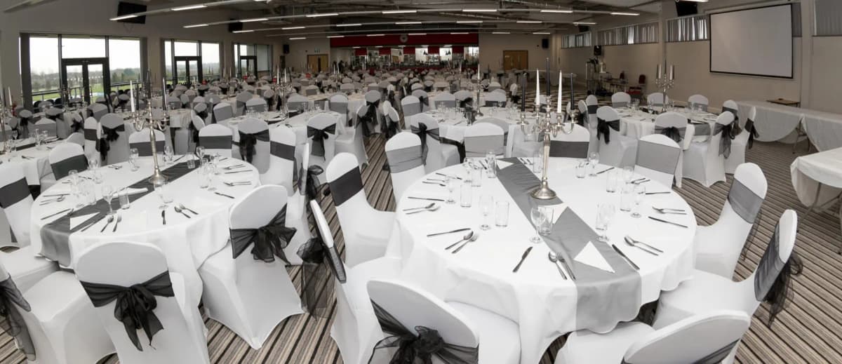 Large banqueting suite laid for a formal dinner with white chair covers and candelabras.