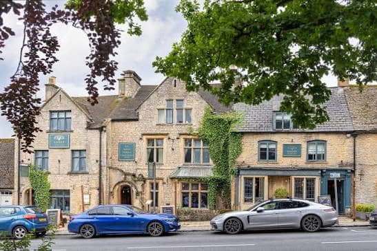 Honey-stone exterior of The Sheep on Sheep Street with ivy-clad walls and parked cars.