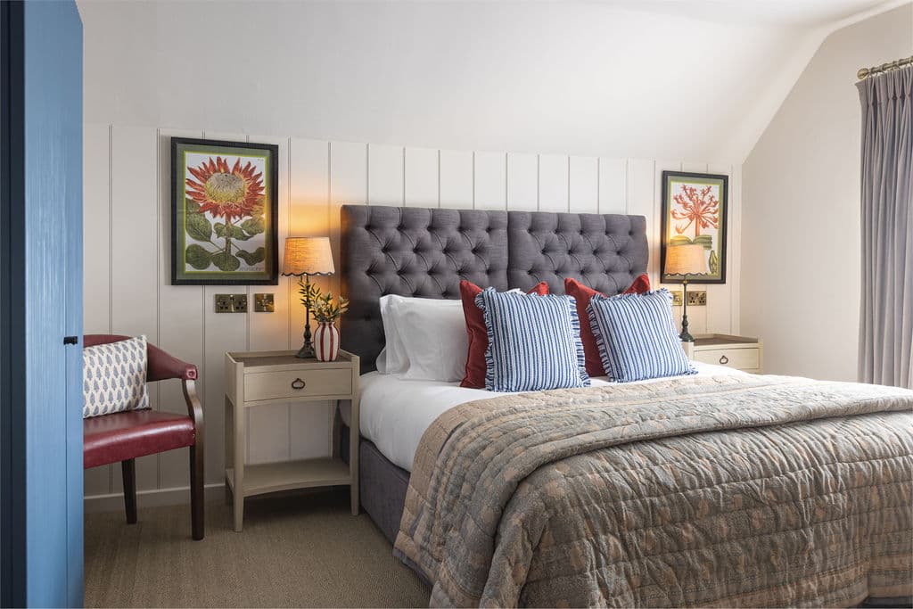 Double bedroom with grey buttoned headboard, blue striped cushions and botanical prints.