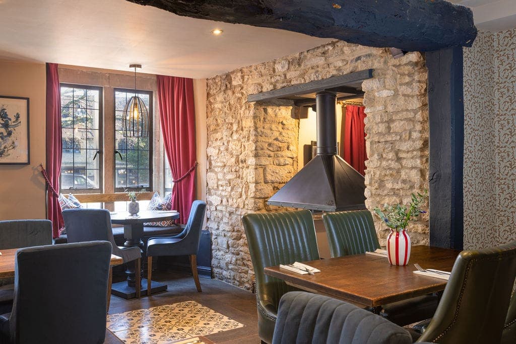 Dining room with stone walls, blue beams, red curtains and leather chairs.