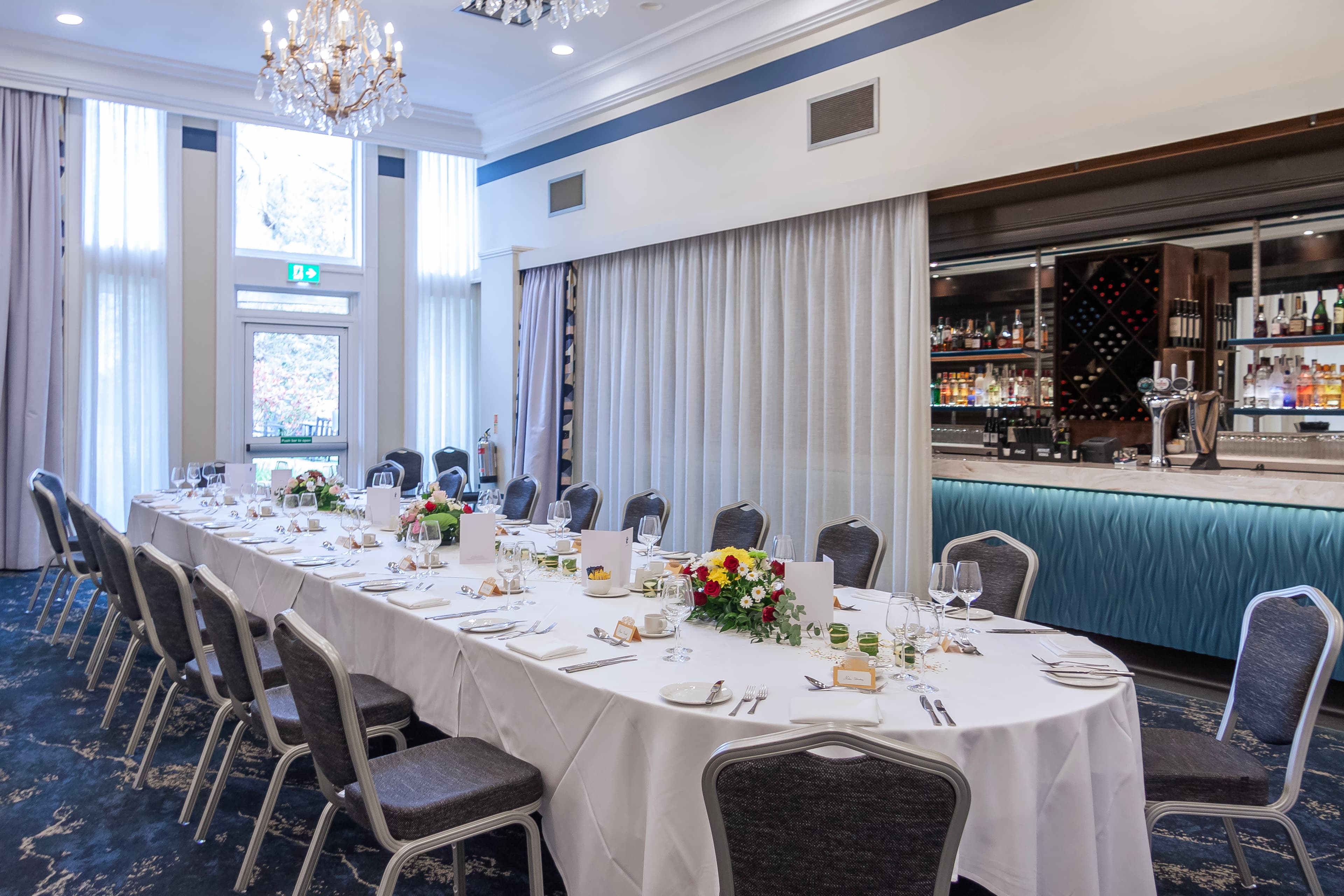Private dining room with a long dressed table, chandelier and adjacent bar at The Spa Hotel.