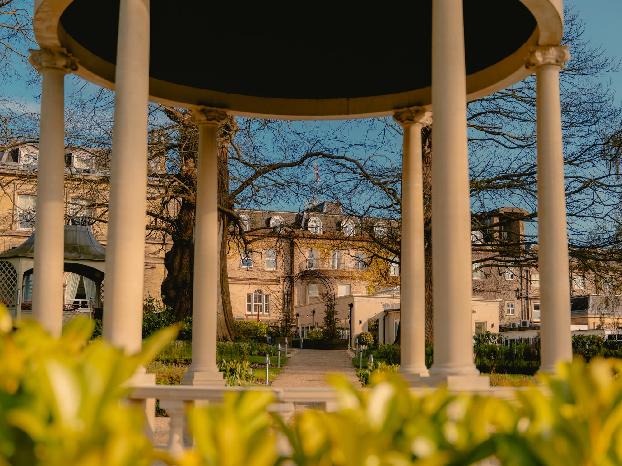 View through a white colonnade rotunda towards The Spa Hotel's Georgian exterior and gardens.
