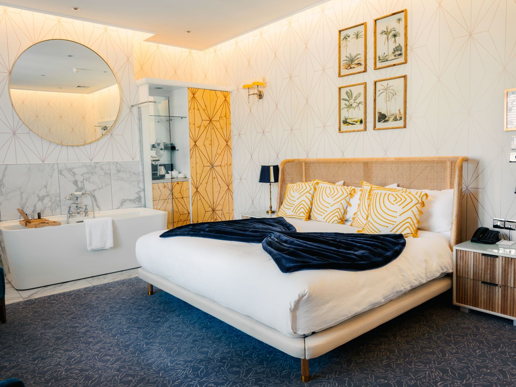 Hotel bedroom with king-size bed, freestanding bath and gold geometric wallpaper.