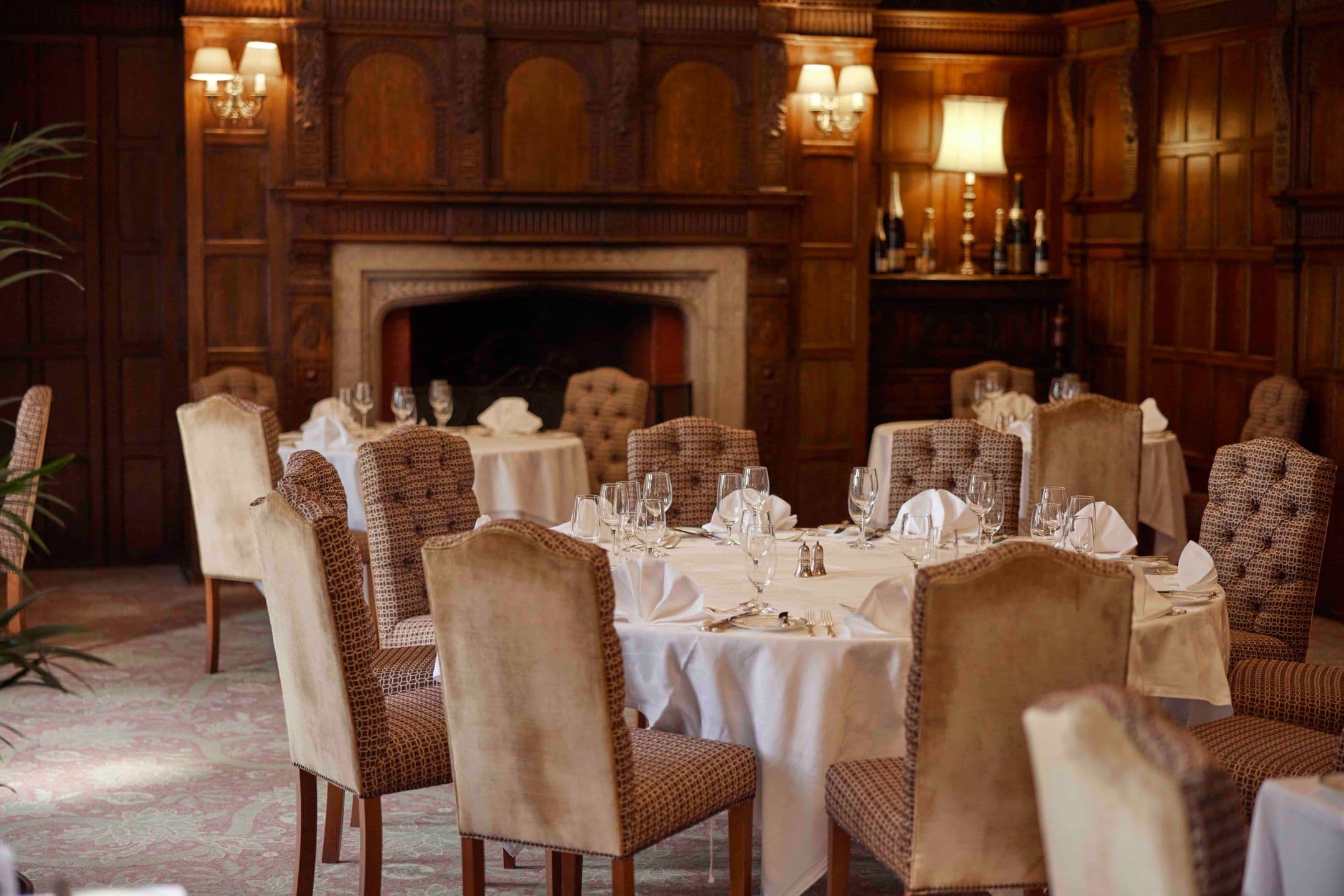 Formal dining room with round tables set for dinner and carved oak panelling