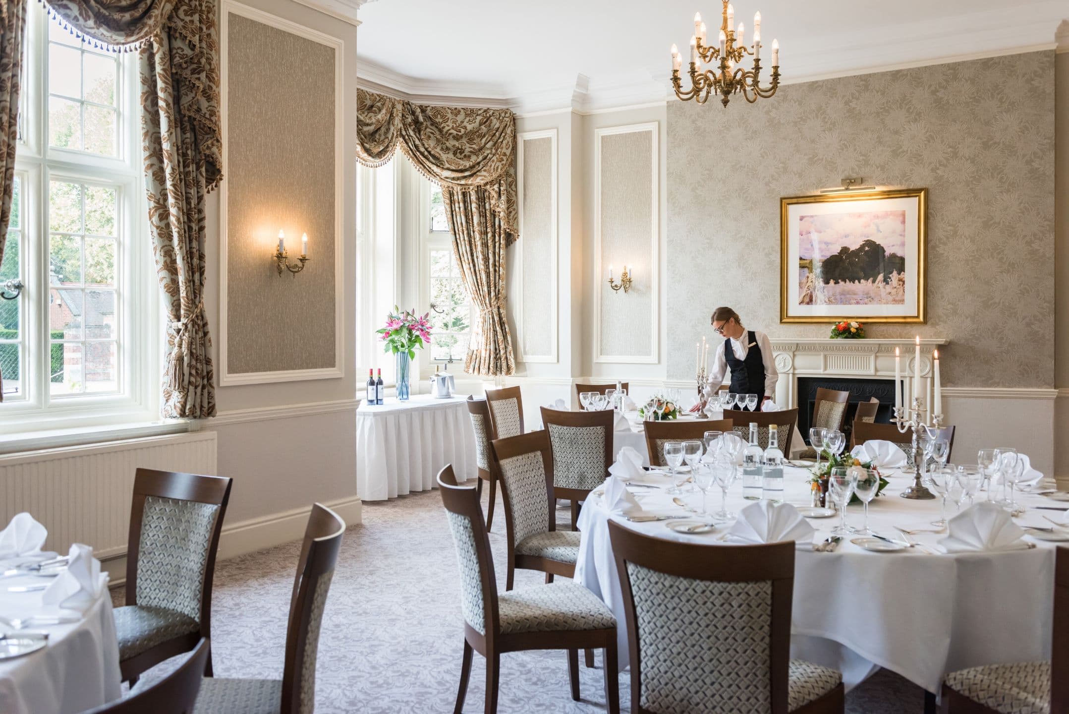 A member of staff laying a formal private dining room with round tables at Tylney Hall Hotel.