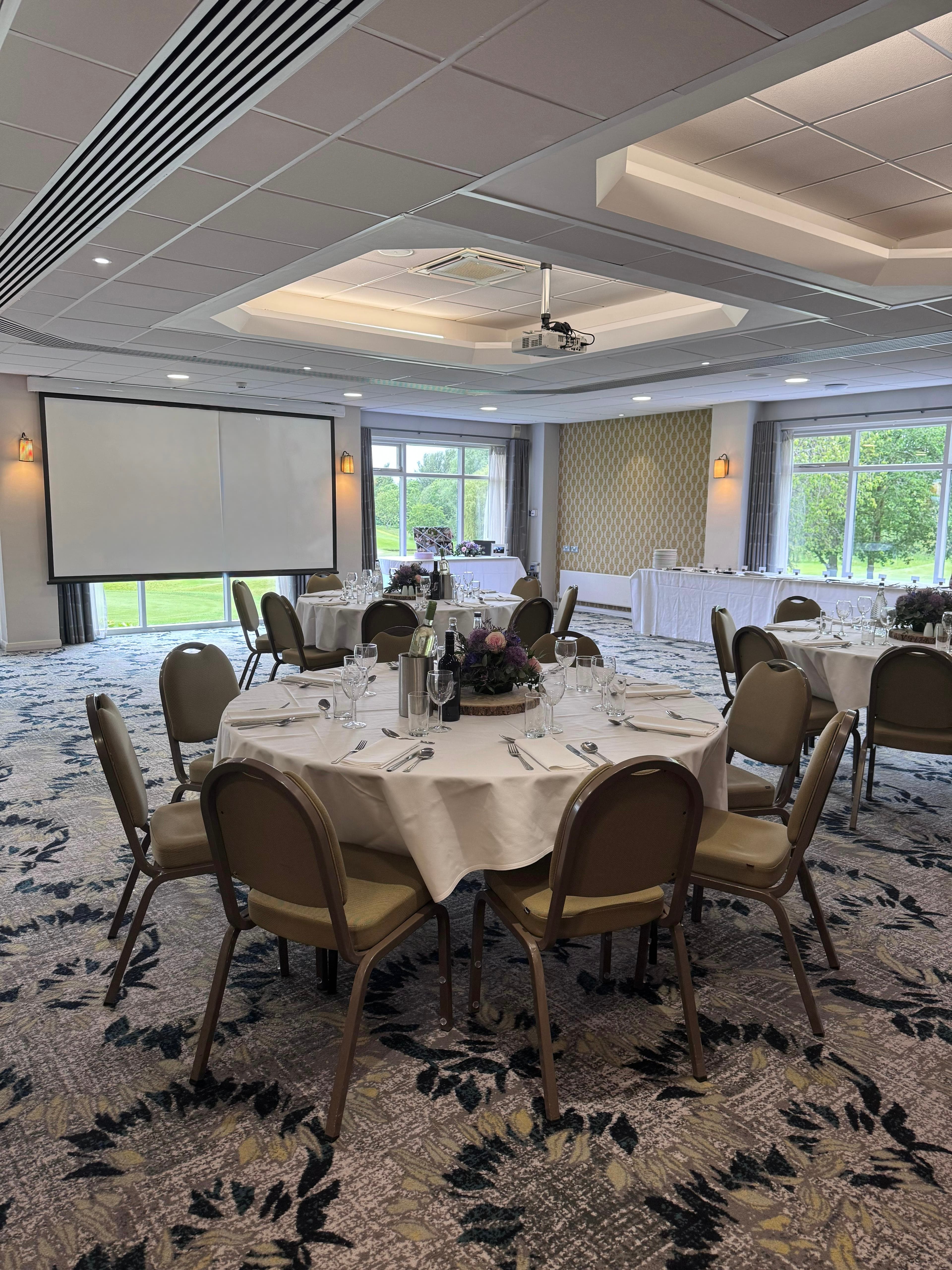 Banqueting room at Tytherington Club with round tables, projector screen and garden views.