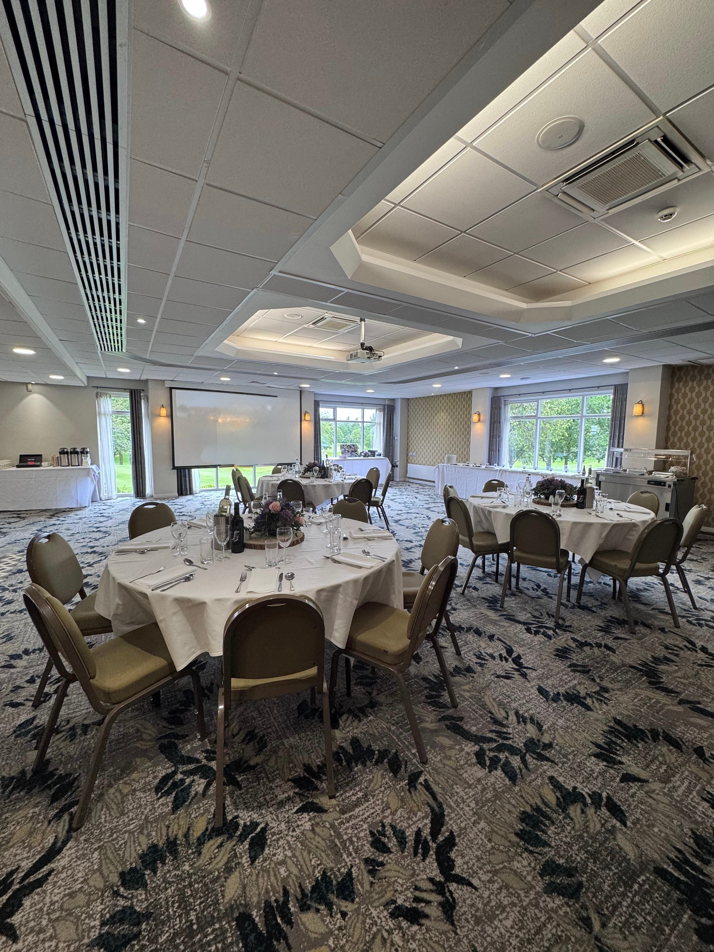 Banqueting room at Tytherington Club with round tables, patterned carpet and projection screen.
