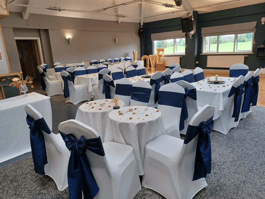 Function room dressed for a wedding with white chair covers and navy sashes.