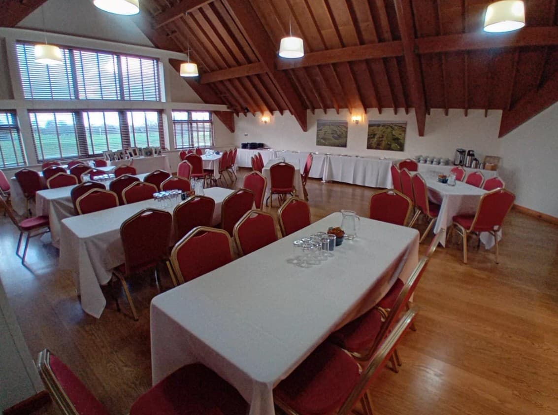 Function room with white-clothed tables, red banquet chairs and exposed timber roof beams.