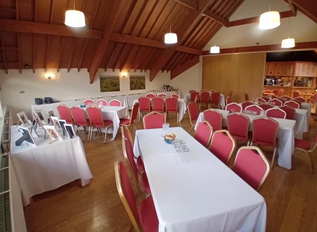 Function room at Weybrook Park Golf Club with white-clothed tables and red banquet chairs.