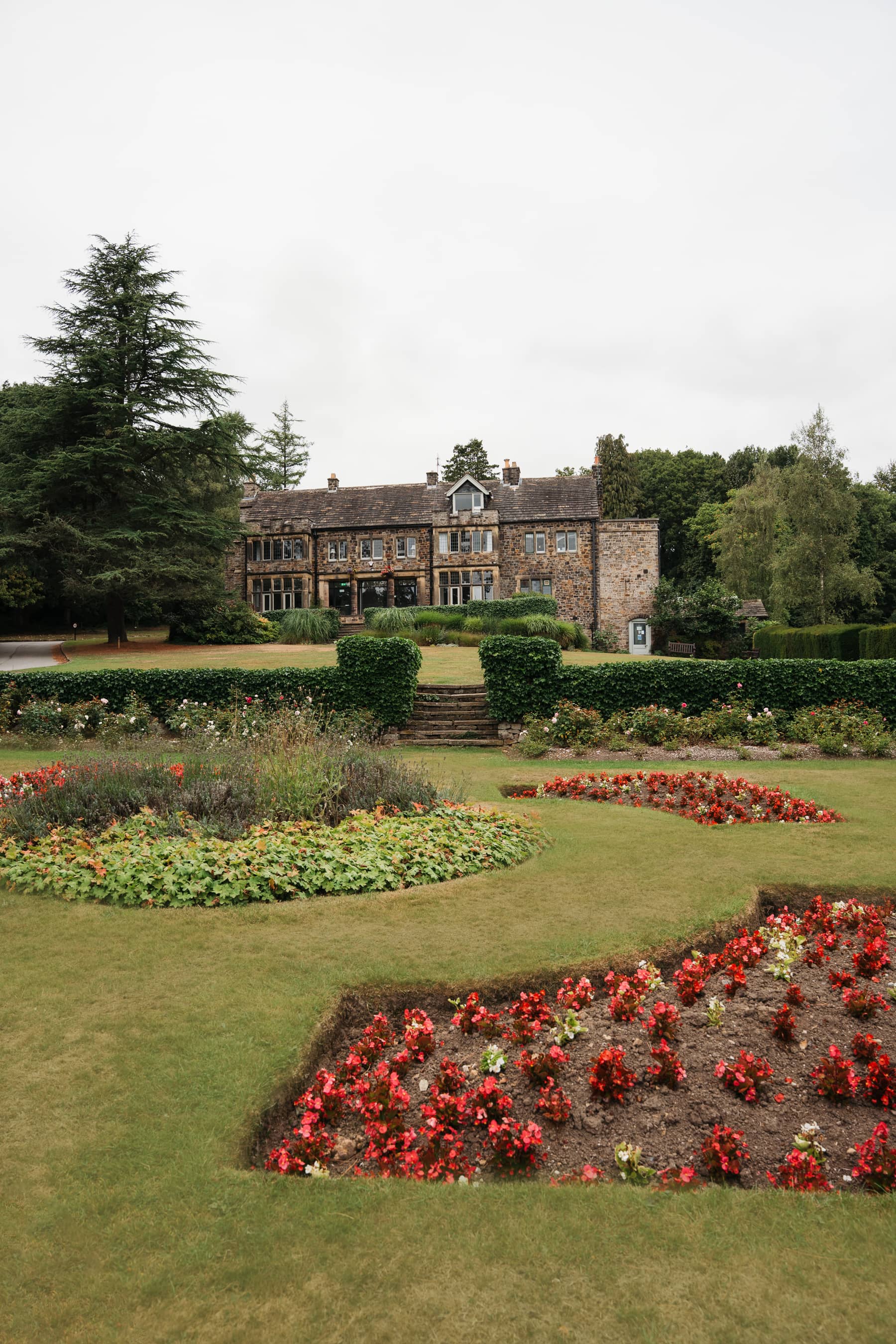 Whirlow Brook Hall exterior seen from formal gardens with red flower beds and manicured lawns.