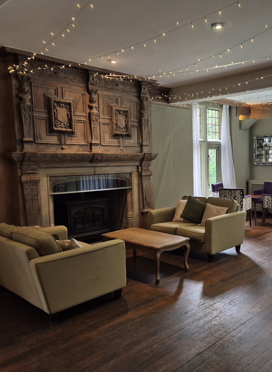 Lounge at Whirlow Brook Hall with ornate stone fireplace, olive sofas and fairy lights.