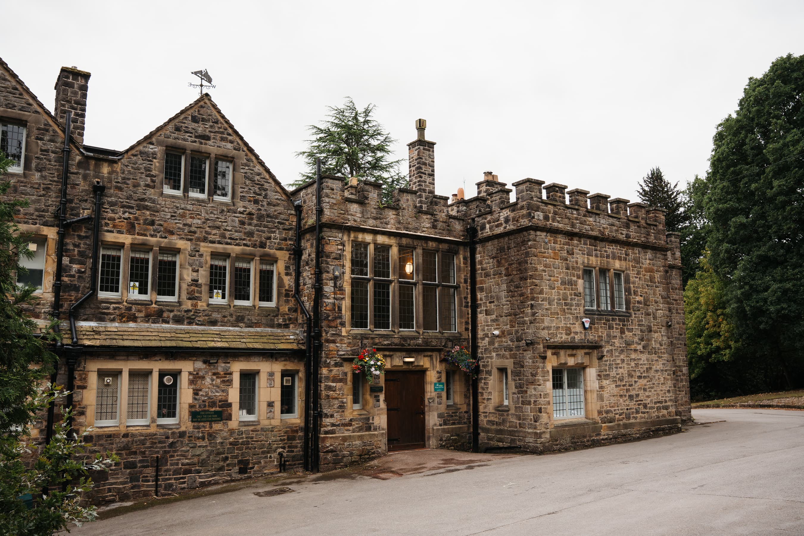 Stone exterior of Whirlow Brook Hall with battlements, leaded windows and hanging baskets.
