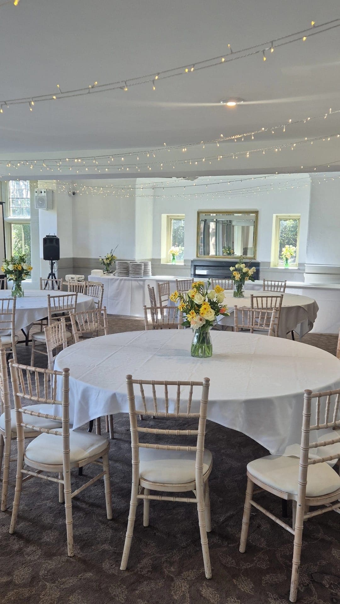 Whirlow Brook Hall function room with round tables, chiavari chairs and fairy lights overhead.