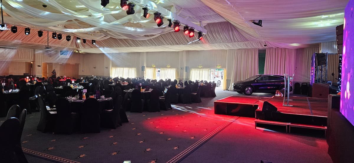 Large function room set for a gala dinner with stage, car display and draped ceiling.